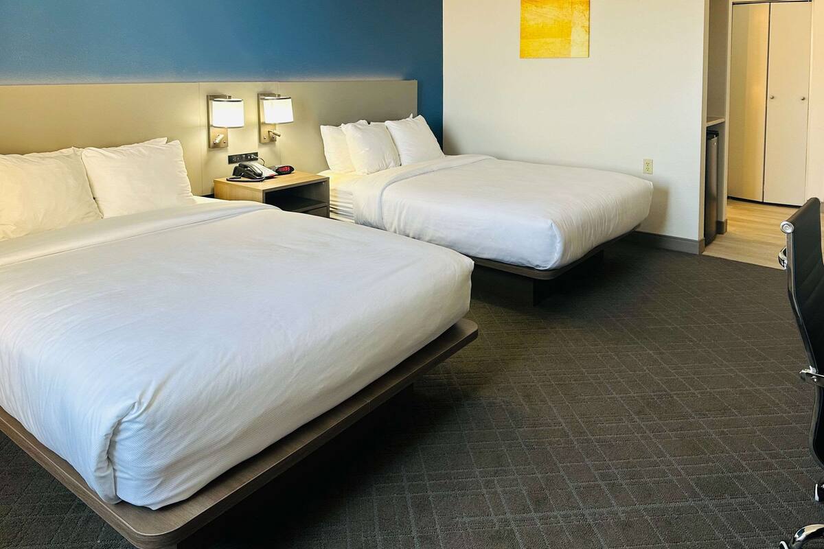 Une chambre d’hôtel avec deux lits, une table de chevet avec un téléphone et une lampe, et une porte donnant sur un placard.