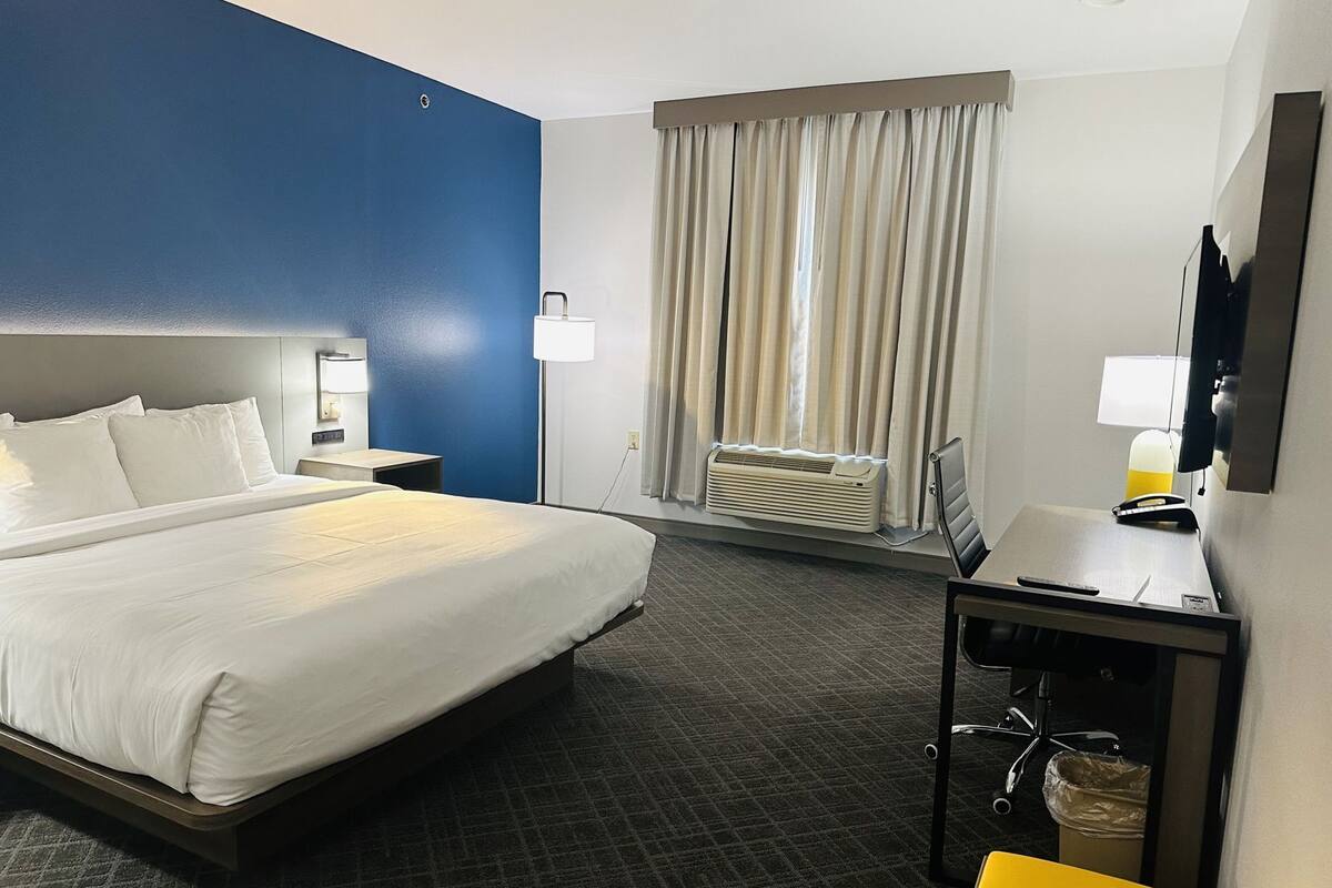 Une chambre d’hôtel équipée d’un lit, d’une table de chevet, d’une lampe, d’un bureau, d’une chaise et d’un appareil de climatisation.