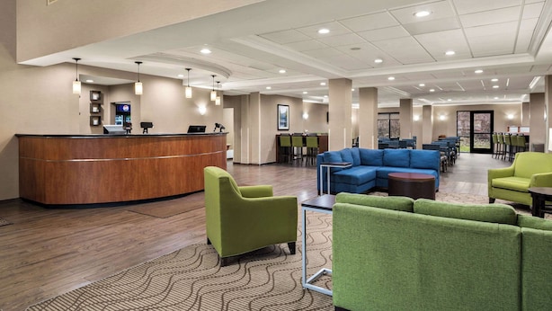 A hotel lobby with a reception desk, green and blue seating areas, and a large window providing natural light. - Comfort Suites Hummelstown - Hershey (Hummelstown)