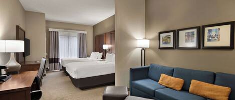 A hotel room with a large bed, a blue sofa, a desk with a lamp, and framed pictures on the wall.