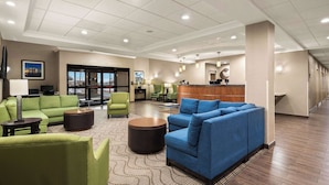 A spacious lobby with green and blue sofas, a reception desk, and a large window offering a view of the outdoors. - Comfort Suites Hummelstown - Hershey (Hummelstown)