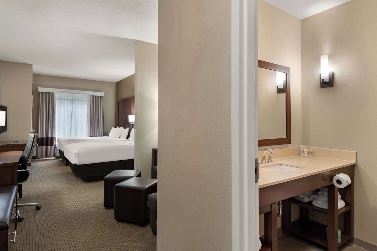 Une chambre d’hôtel équipée d’un lit, d’un bureau, d’une chaise, d’un grand miroir, d’un lavabo et de toilettes.