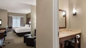 A hotel room with a bed, a desk, a chair, a large mirror, a sink, and a toilet.