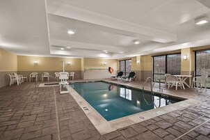 An indoor swimming pool with a tiled floor, poolside chairs, and a lifeguard chair.