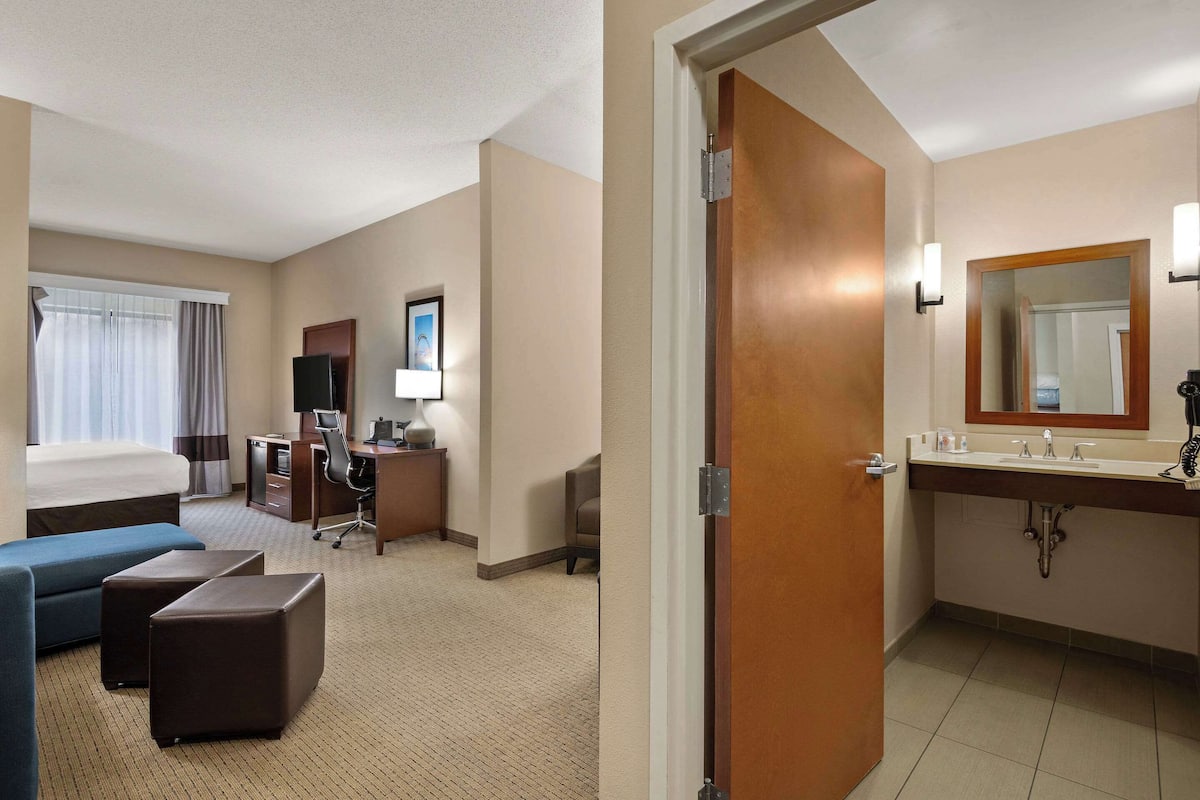 Une chambre d’hôtel comprenant un lit, un bureau, une chaise, un canapé et une salle de bain avec un lavabo et un miroir.