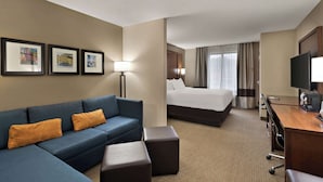 A hotel room with a blue sofa, a bed, a desk with a TV, and framed pictures on the wall. - Comfort Suites Hummelstown - Hershey (Hummelstown)