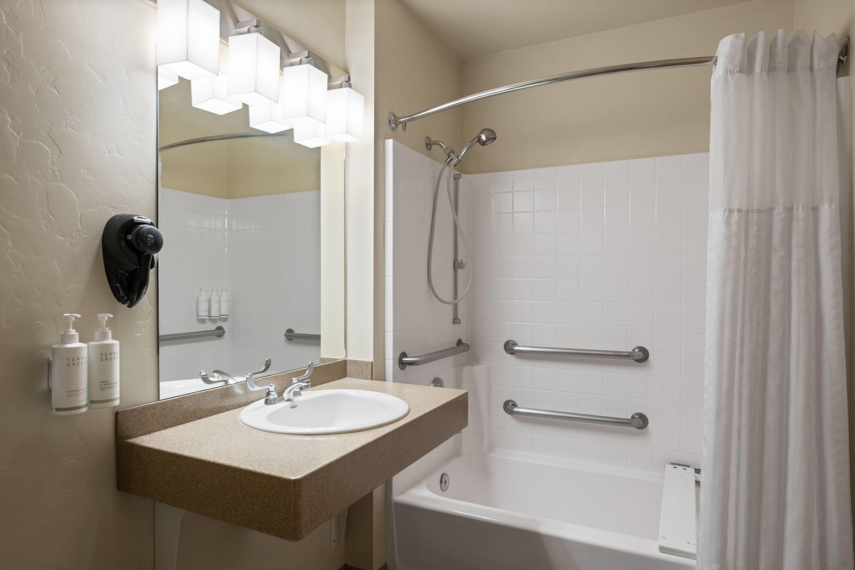 A bathroom with a sink, mirror, shower, and bathtub.