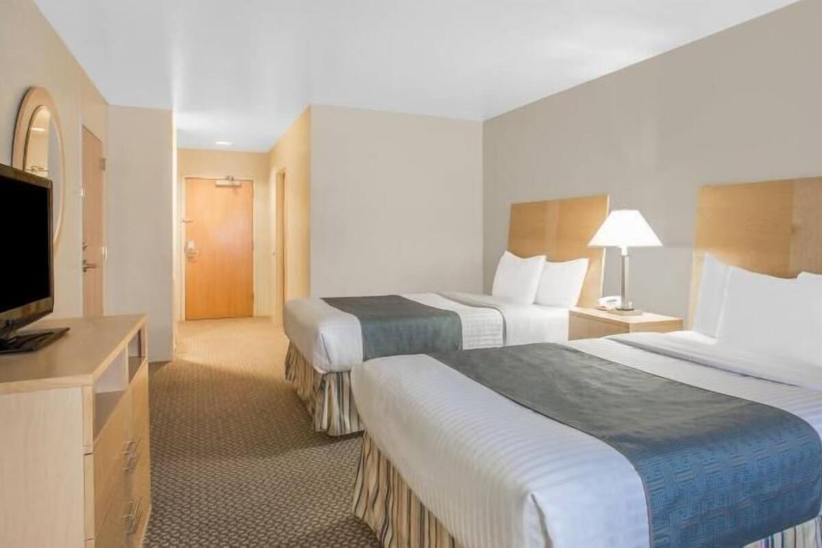 A hotel room with two beds, a TV, a desk, and a lamp.