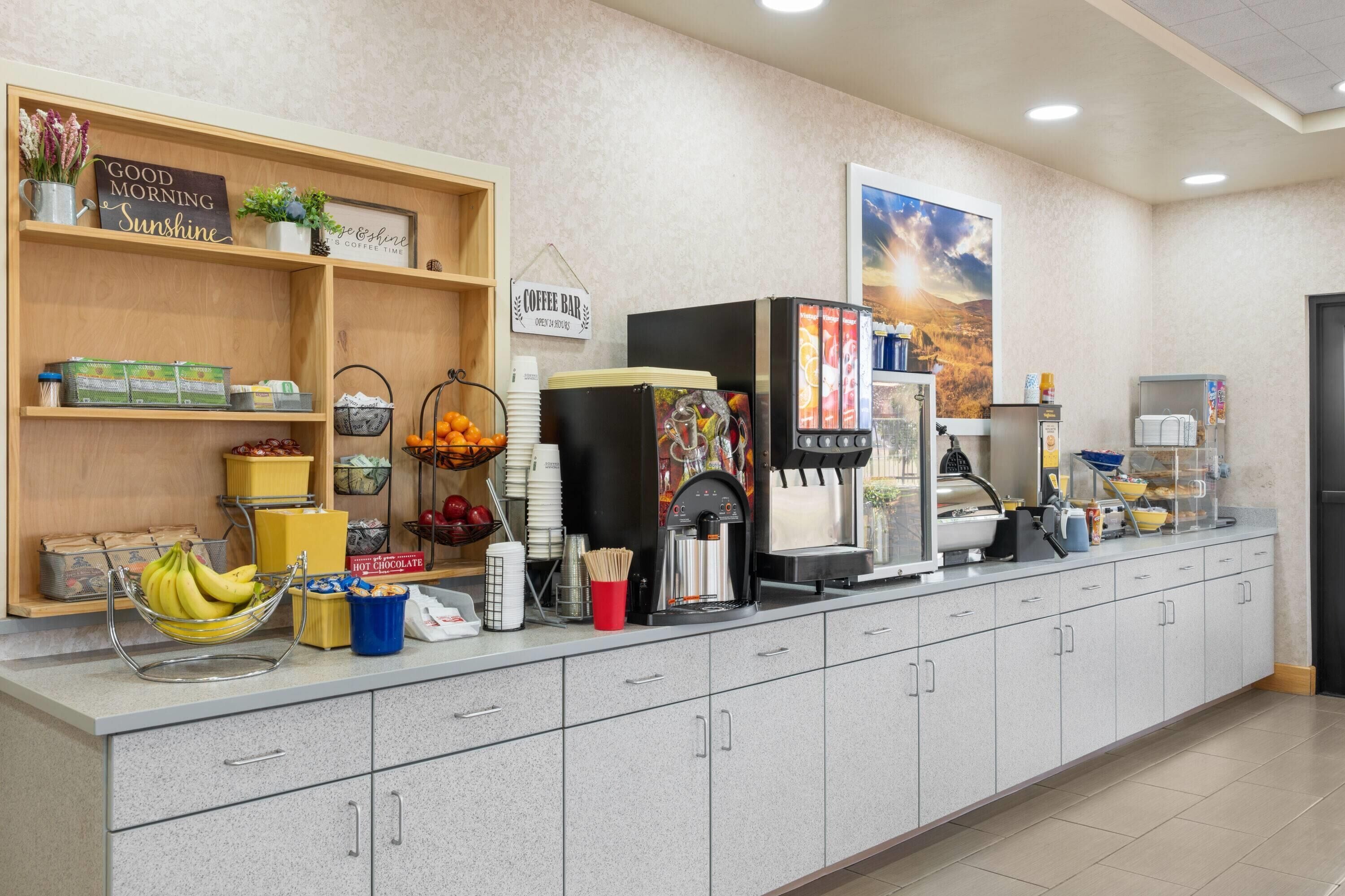 A breakfast bar with a coffee machine, fruit bowl, and various food items.