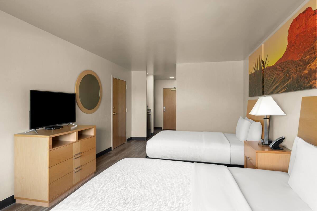 A hotel room with a bed, a TV, a desk with drawers, a lamp, and a painting on the wall.