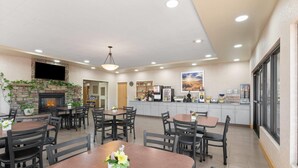 A restaurant with multiple tables and chairs, a stone fireplace, a flat-screen TV, and a kitchen area with appliances. - Days Inn by Wyndham Chino Valley (Chino Valley)
