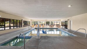 An indoor swimming pool with clear glass walls, a tiled floor, and a seating area with chairs and tables. - Days Inn by Wyndham Chino Valley (Chino Valley)