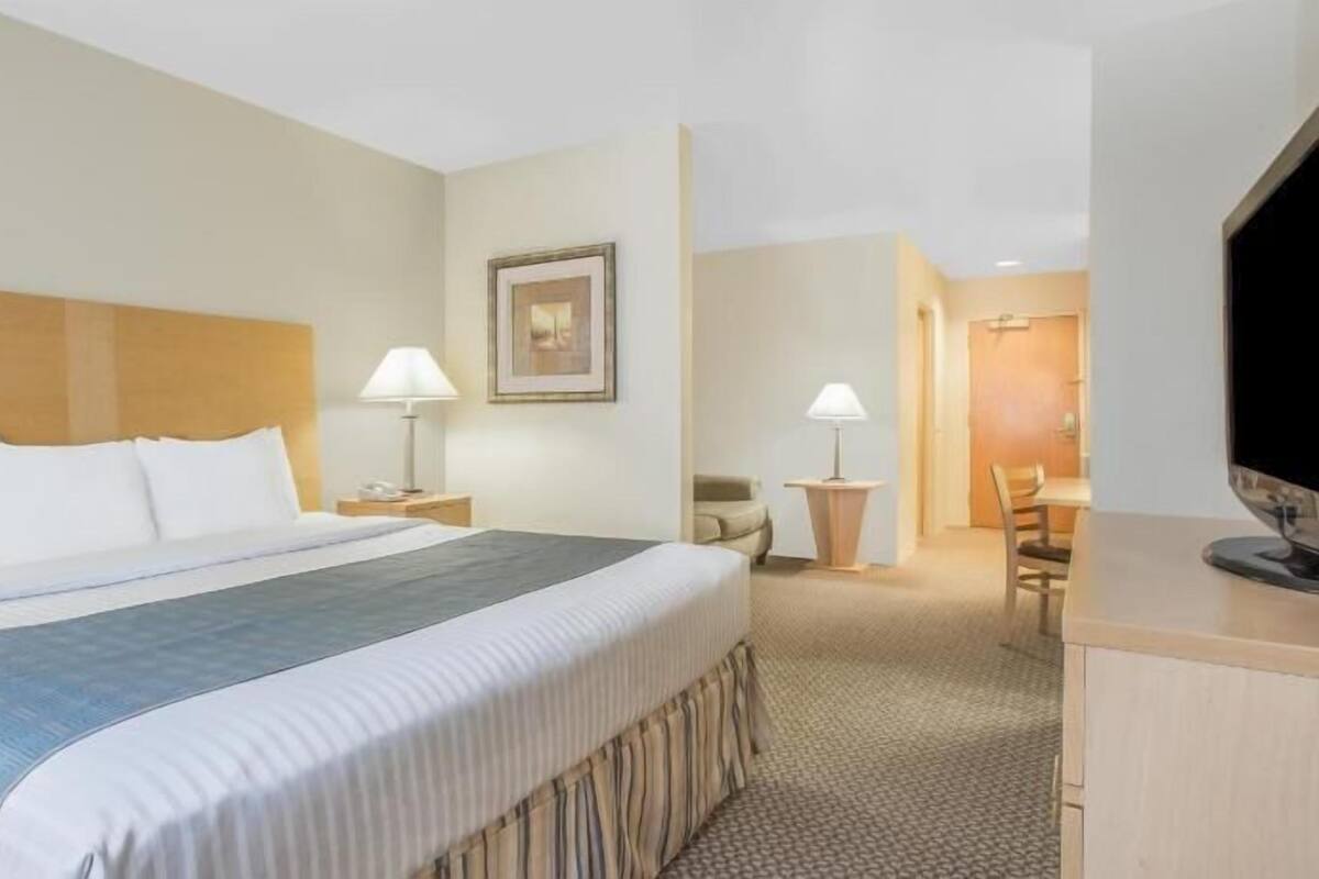 A hotel room with a large bed, bedside lamps, a desk, a chair, and a television.