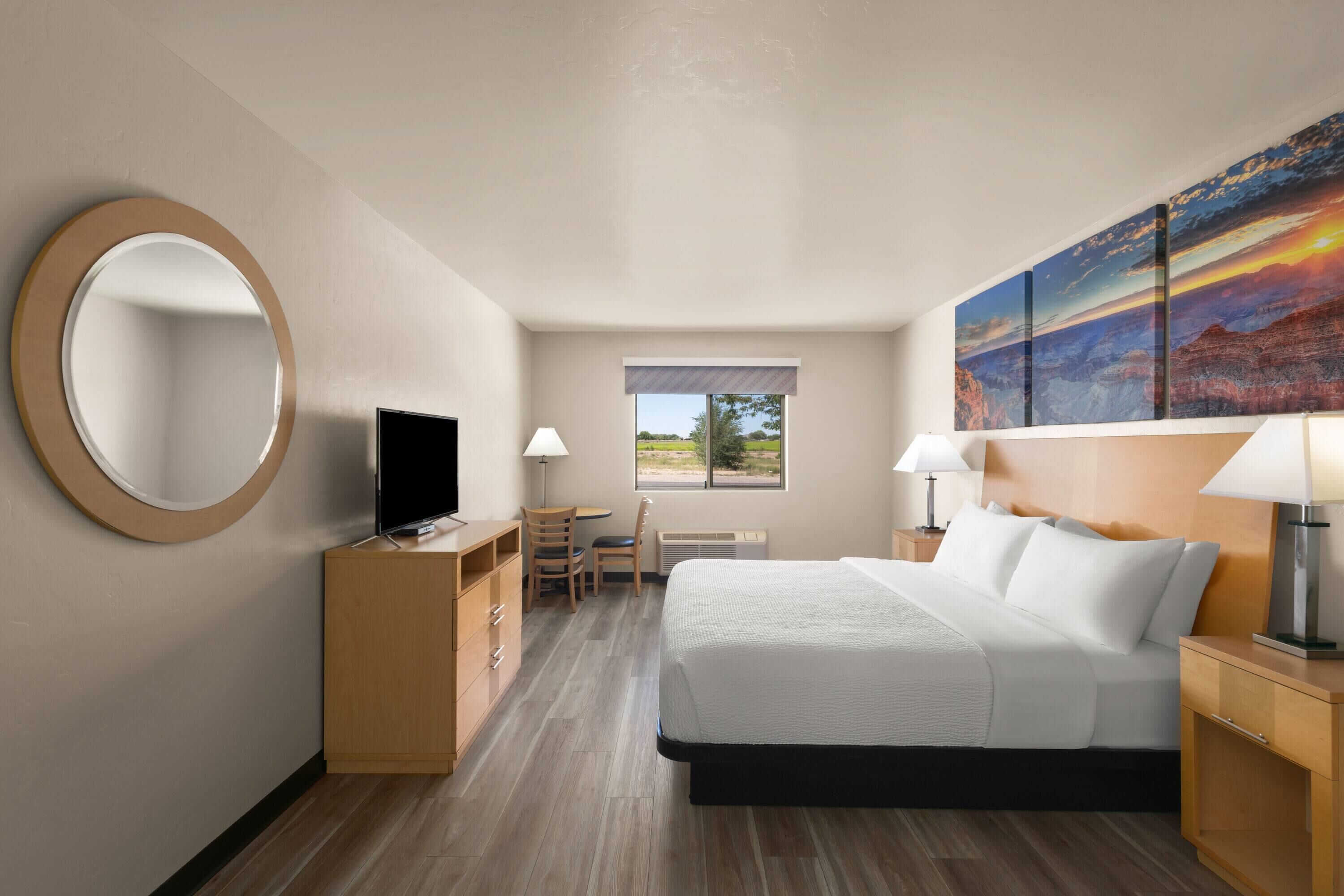 A hotel room with a bed, a desk, a chair, a TV, and a large painting on the wall.
