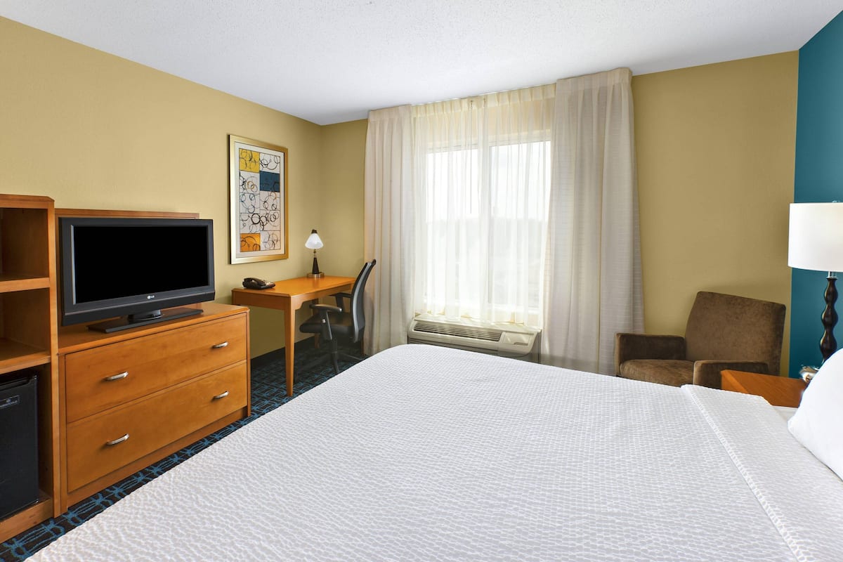 A hotel room with a bed, a desk with a chair, a television, and a window with curtains.