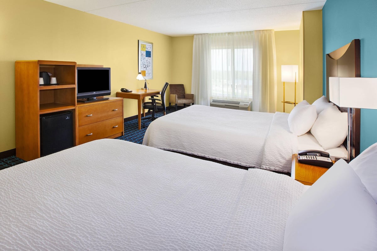 A hotel room with two beds, a desk with a TV, a mini-fridge, a chair, and a lamp.