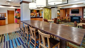 A modern hotel lobby with a long wooden bar, multiple seating areas, and a television mounted on the wall. - Fairfield Inn & Suites by Marriott Lexington North (Lexington)