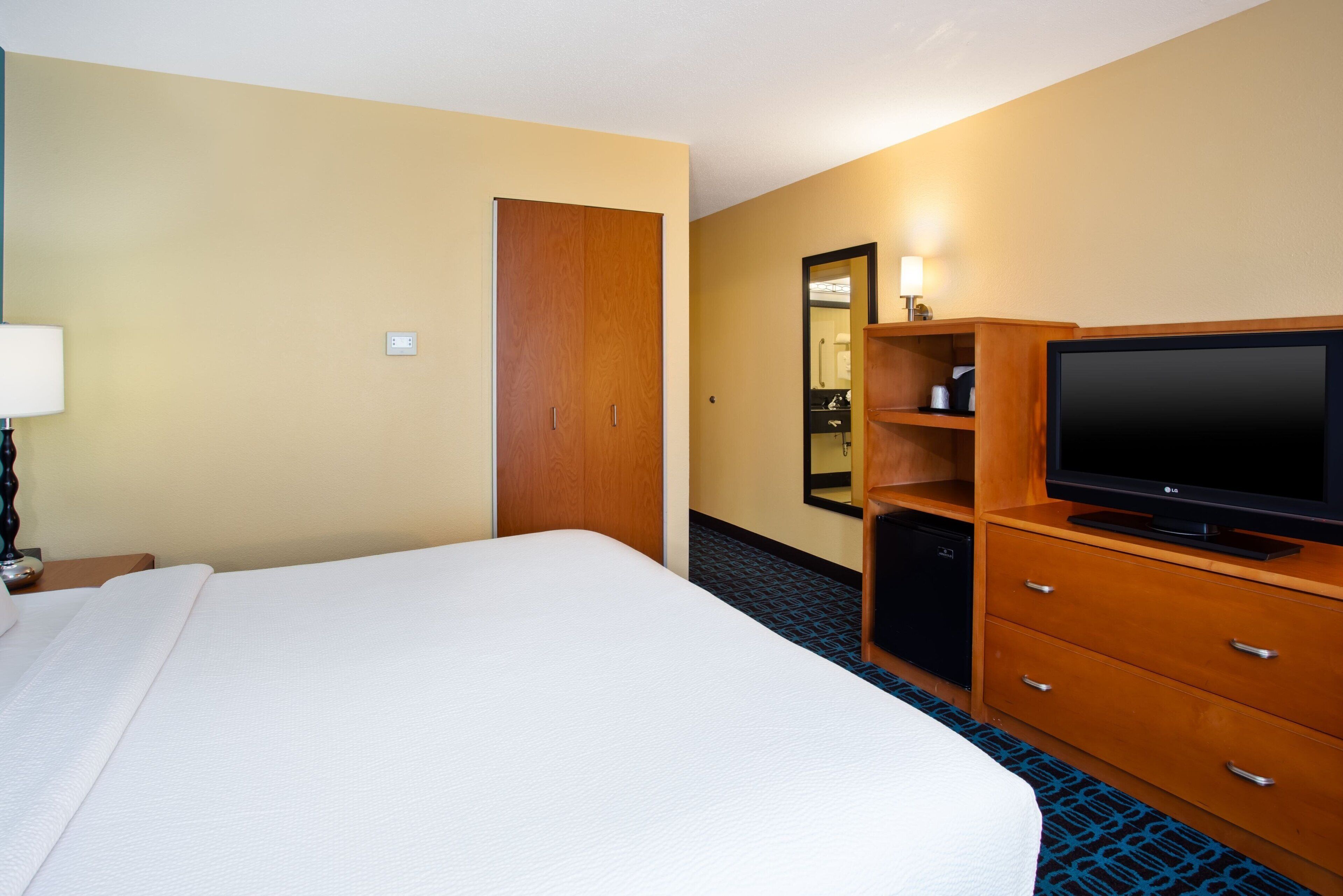 Quarto de hotel com uma cama grande, cómoda de madeira, televisão e espelho.