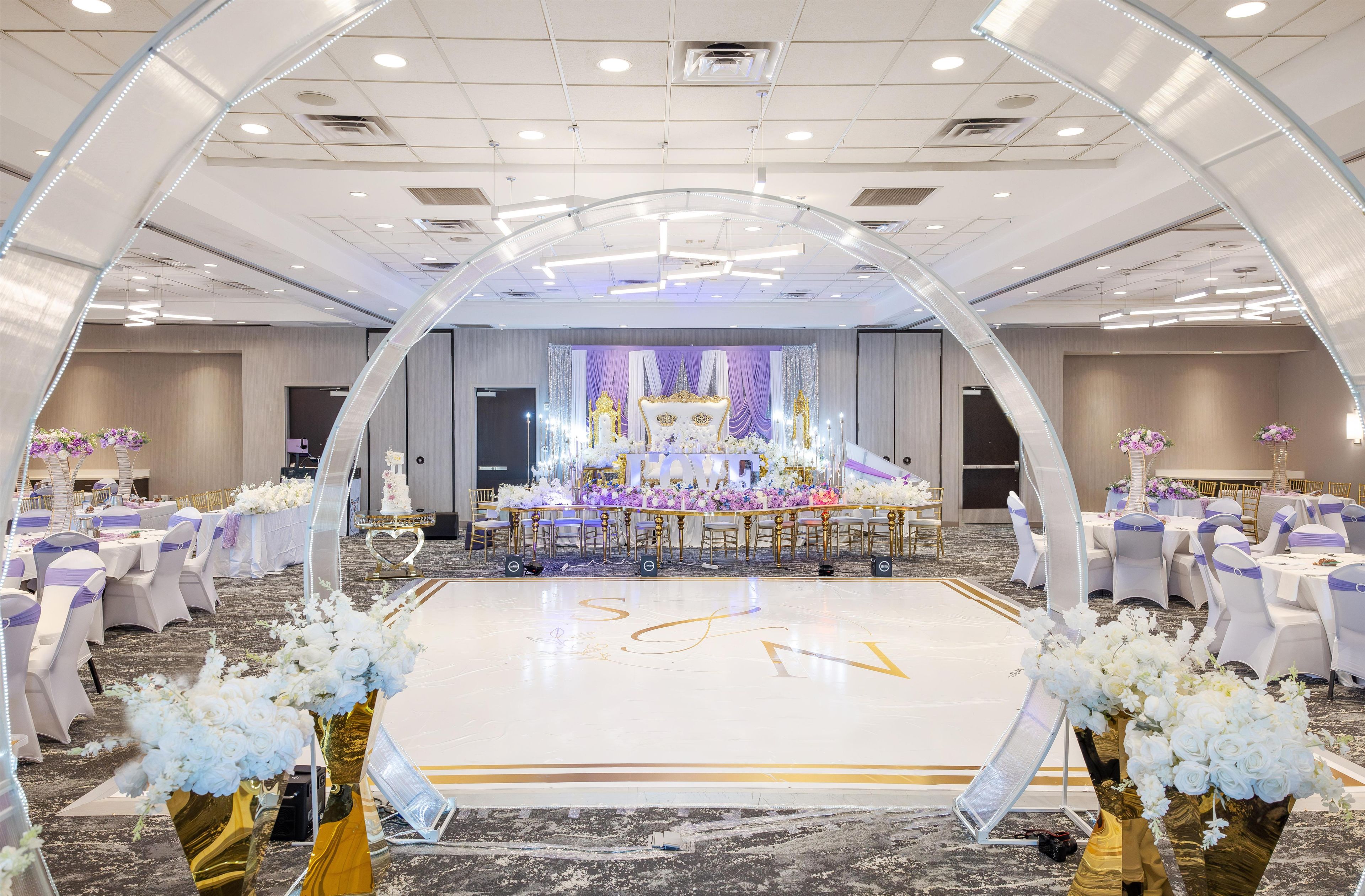 Une cérémonie de mariage avec une arche transparente, une scène décorée de compositions florales et des tables avec des chaises disposées pour les invités.