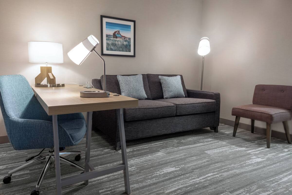 A modern room with a desk, a grey sofa, a blue office chair, and two floor lamps.