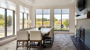 Un comedor con una mesa grande y sillas, ventanas amplias con vistas al exterior, una chimenea y una lámpara en el techo.