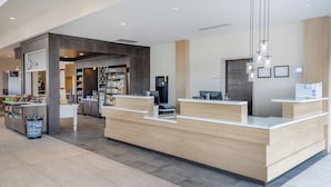 Un área de recepción moderna con un mostrador de madera, una máquina de café y un refrigerador.