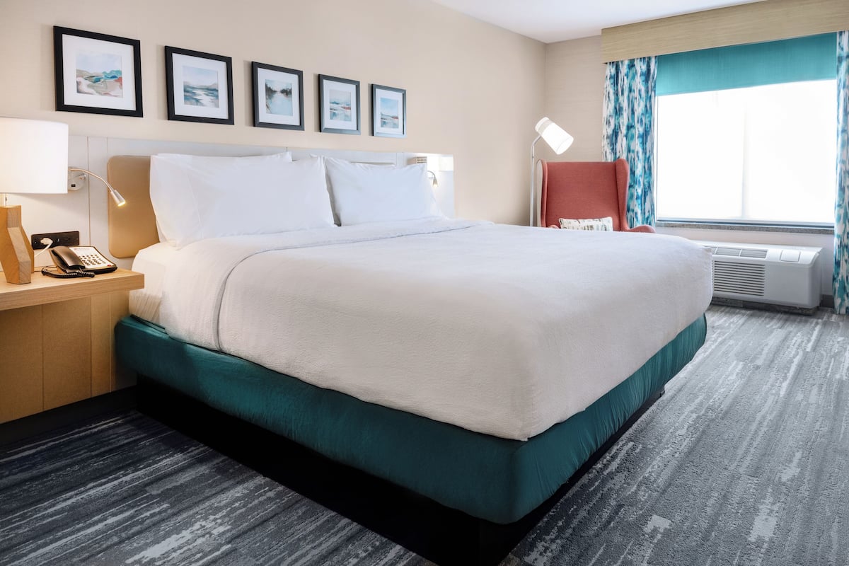 A hotel room with a large bed, a desk with a telephone, framed pictures on the wall, and a window with curtains.