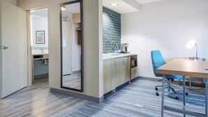 A modern kitchen with a blue chair and a table, a mirror, and a view into another room.