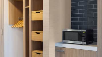 A kitchen with a microwave on the counter, wooden cabinets, and a hanging rack with wooden utensils.