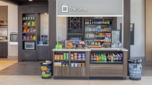 Una tienda llamada 'The Shop' con una sección refrigerada, estantes llenos de snacks y un basurero.