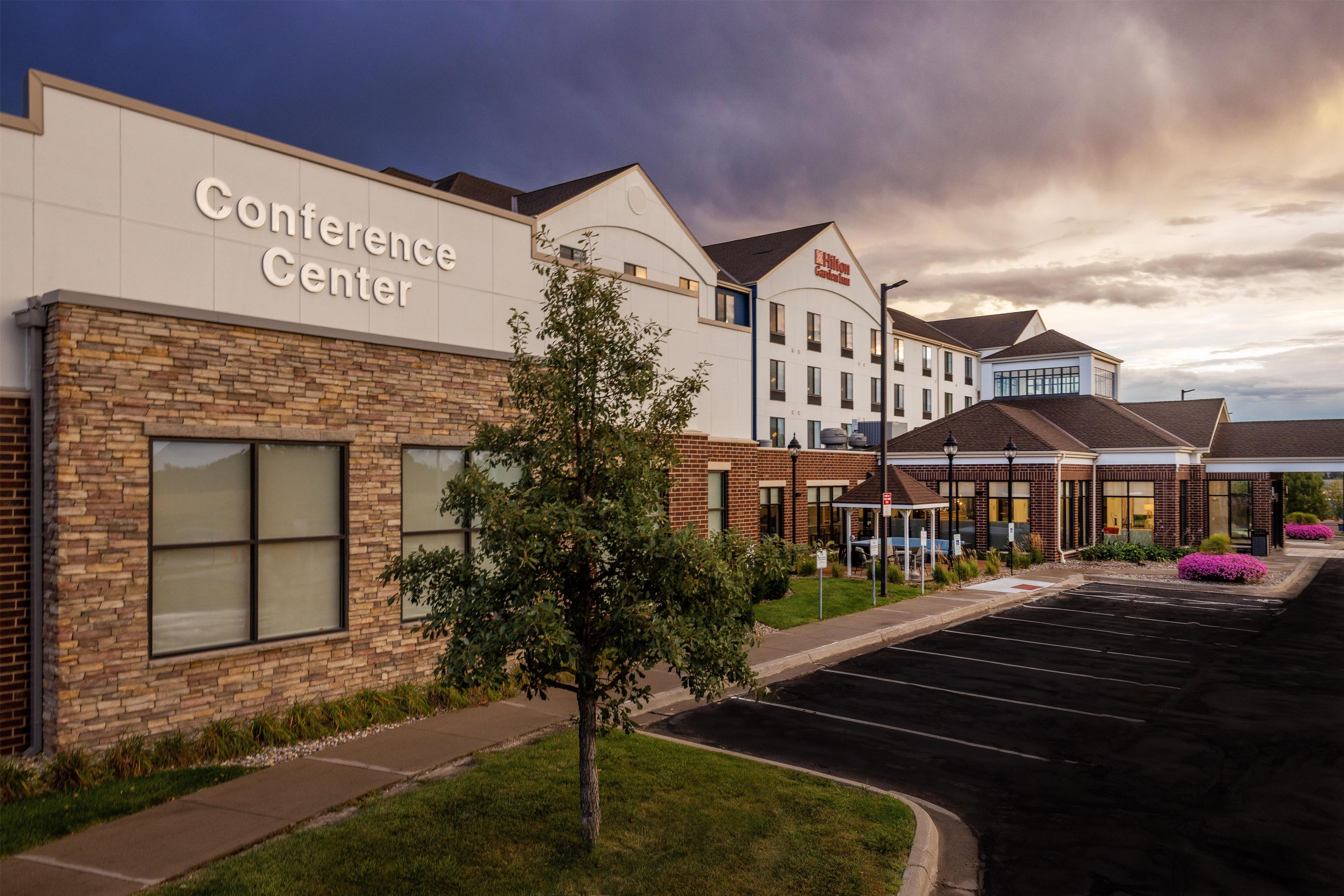 A hotel with a conference center, a parking lot, and a landscaped area with trees.