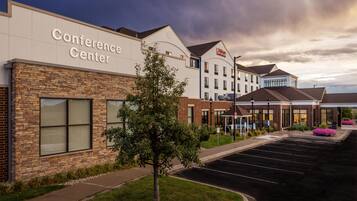 A hotel with a conference center, a parking lot, and a landscaped area with trees.