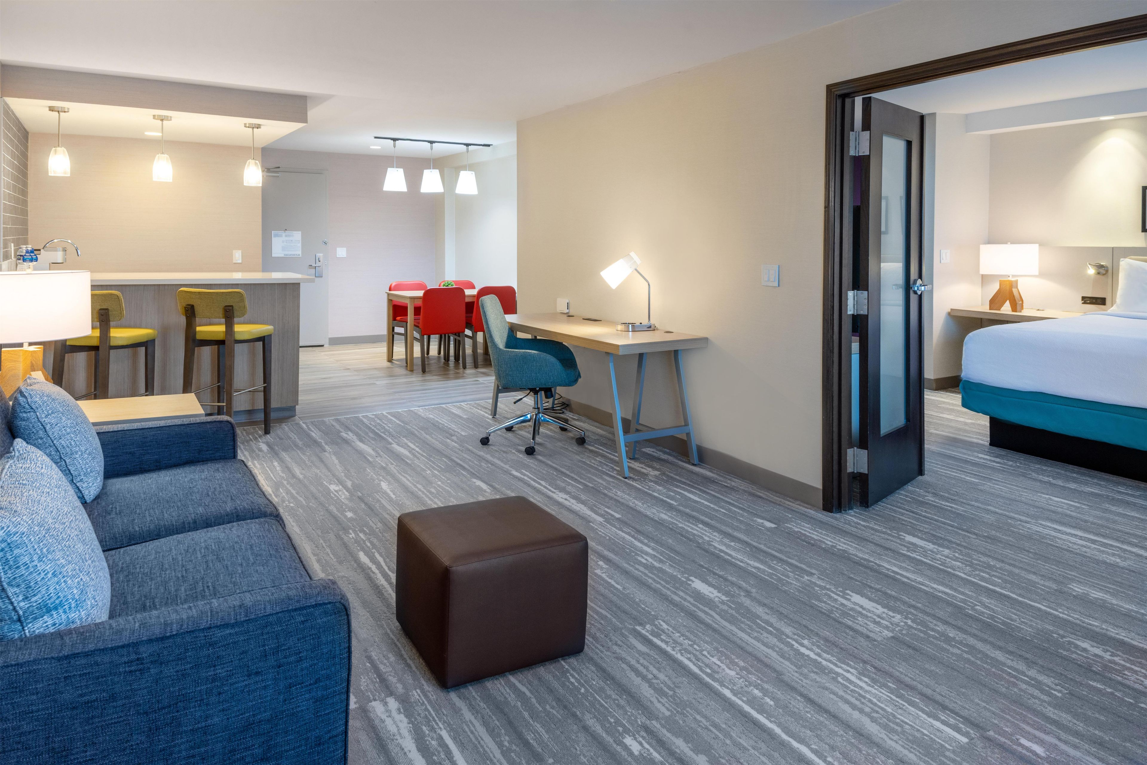 A hotel room with a bed, a desk, a chair, a sofa, and a small ottoman.