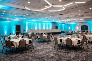 A large conference room with multiple round tables and chairs, a stage with curtains, and a carpeted floor. - Hilton Garden Inn Sioux Falls South (Sioux Falls)
