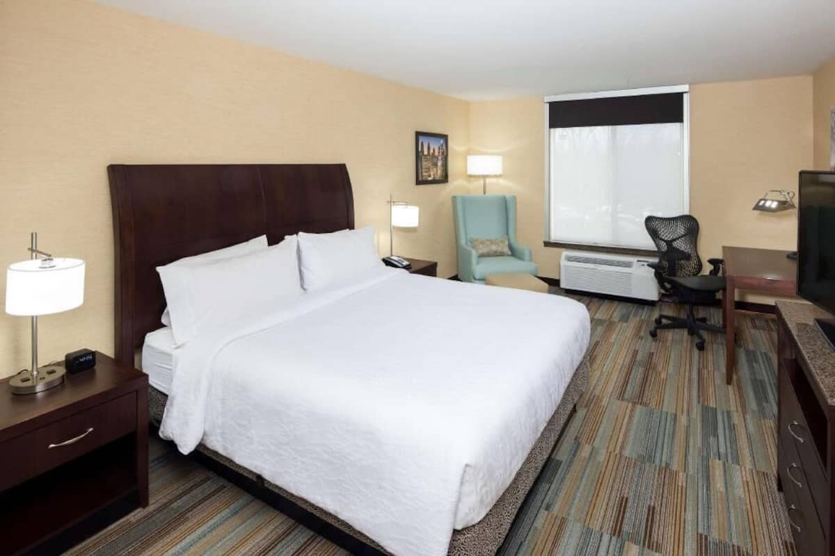 Una habitación de hotel con una cama grande, un escritorio, una silla, una lámpara y una ventana.