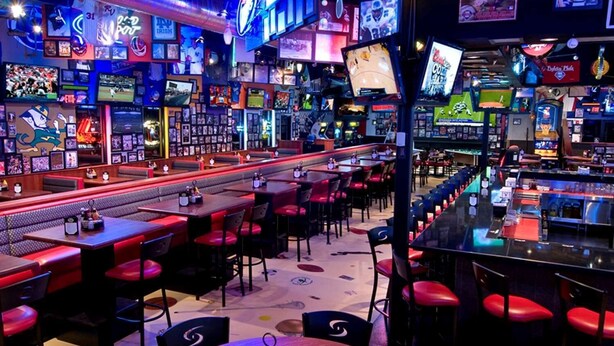 A bar with multiple screens, red seating, and various sports memorabilia. - Hilton Garden Inn Mount Holly/Westampton (Mount Holly)