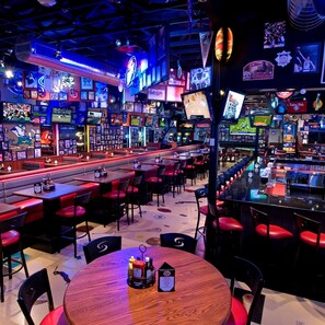 A bar with multiple screens, red seating, and various sports memorabilia. - Hilton Garden Inn Mount Holly/Westampton (Mount Holly)