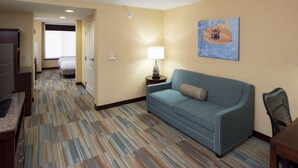 A hotel room with a blue sofa, a lamp, a painting on the wall, and a carpeted floor. - Hilton Garden Inn Mount Holly/Westampton (Mount Holly)