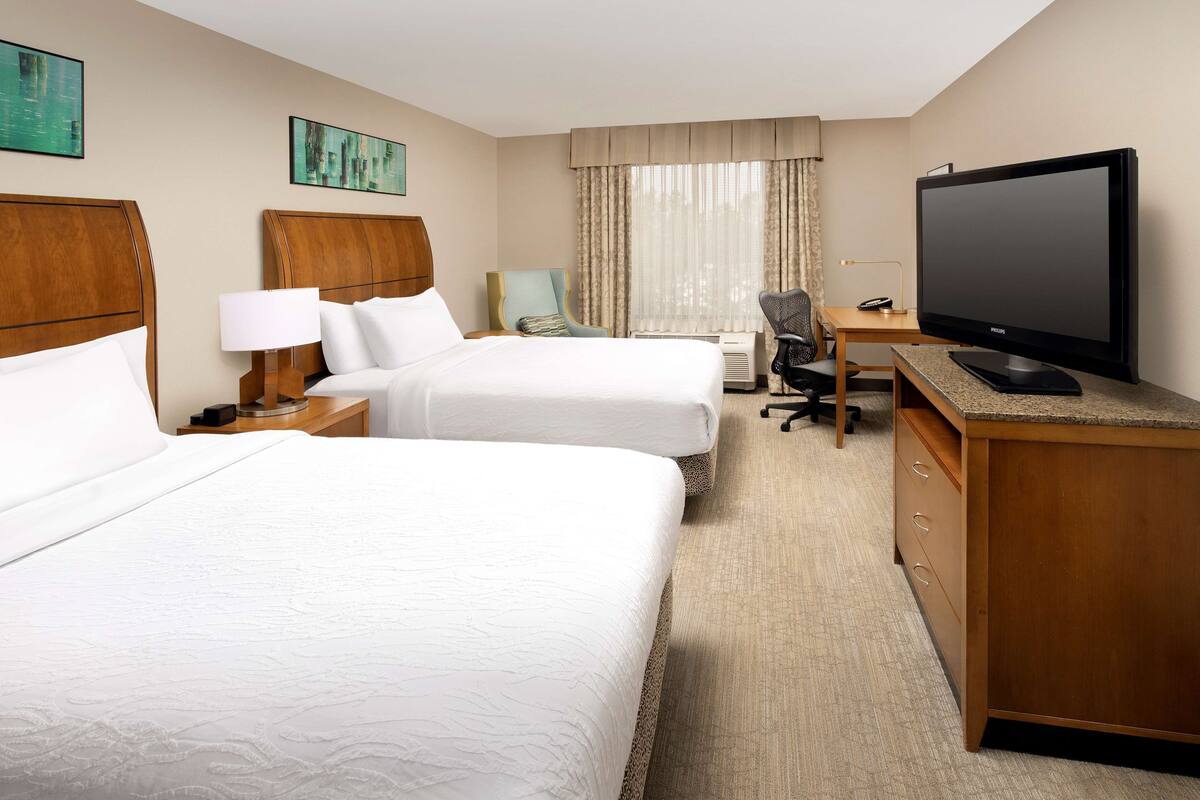 A hotel room with two beds, a desk with a television, and a chair.