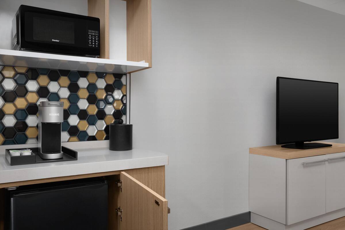 A modern kitchen with a microwave, coffee maker, and a flat-screen TV on a wooden cabinet.