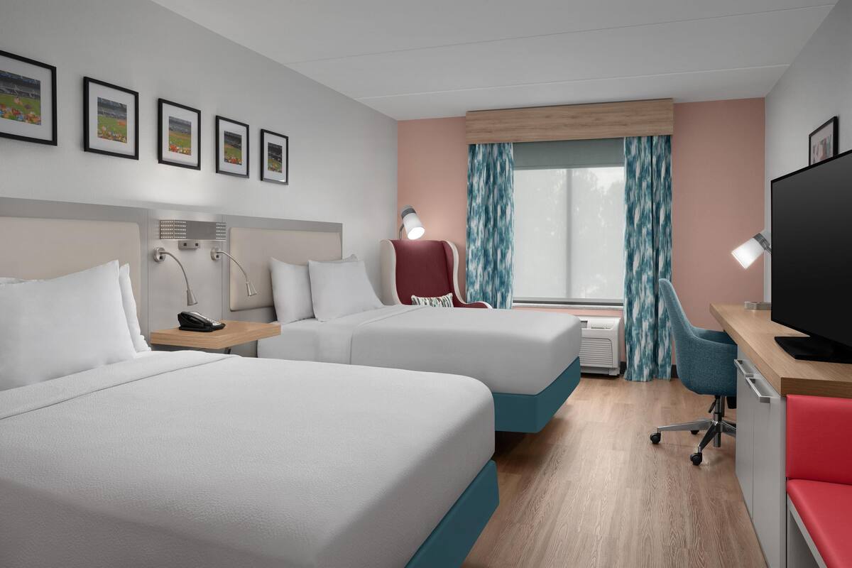 A hotel room with two beds, a desk, a TV, and a window with curtains.