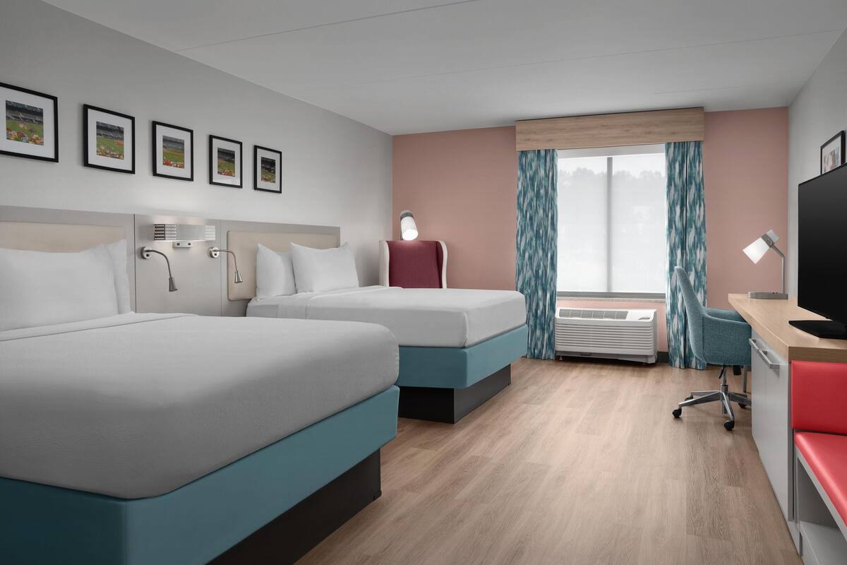 A hotel room with two beds, a desk, a TV, and a window with curtains.