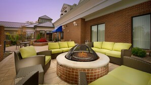 An outdoor patio area with a fire pit, green cushioned seating, and a brick wall.
