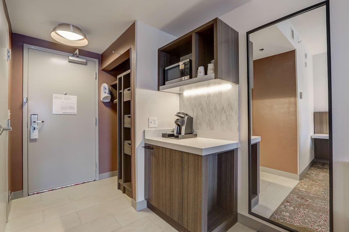 A modern hotel room with a wooden cabinet, a microwave, and a coffee machine on the counter.