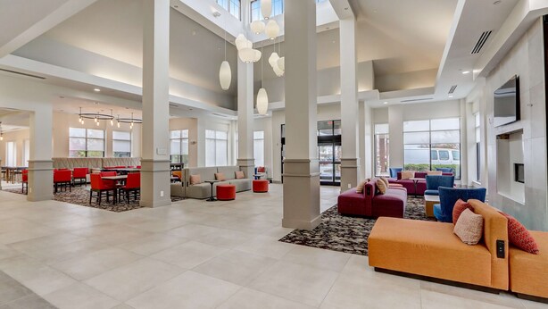 A spacious hotel lobby with high ceilings, large windows, and modern furnishings including a red sofa and multiple seating areas.