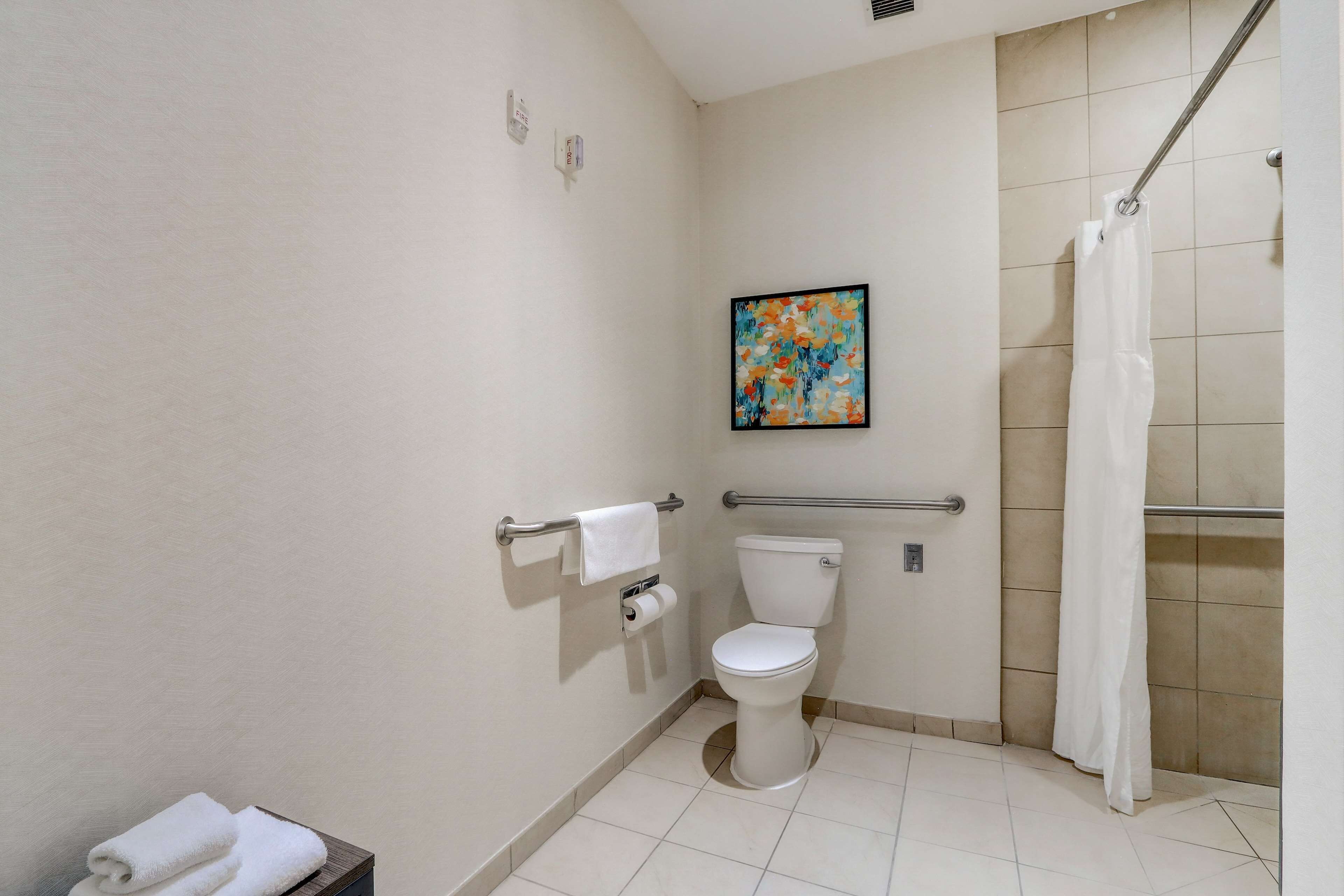 A bathroom with a toilet, a handrail, a shower curtain, and a towel rack.