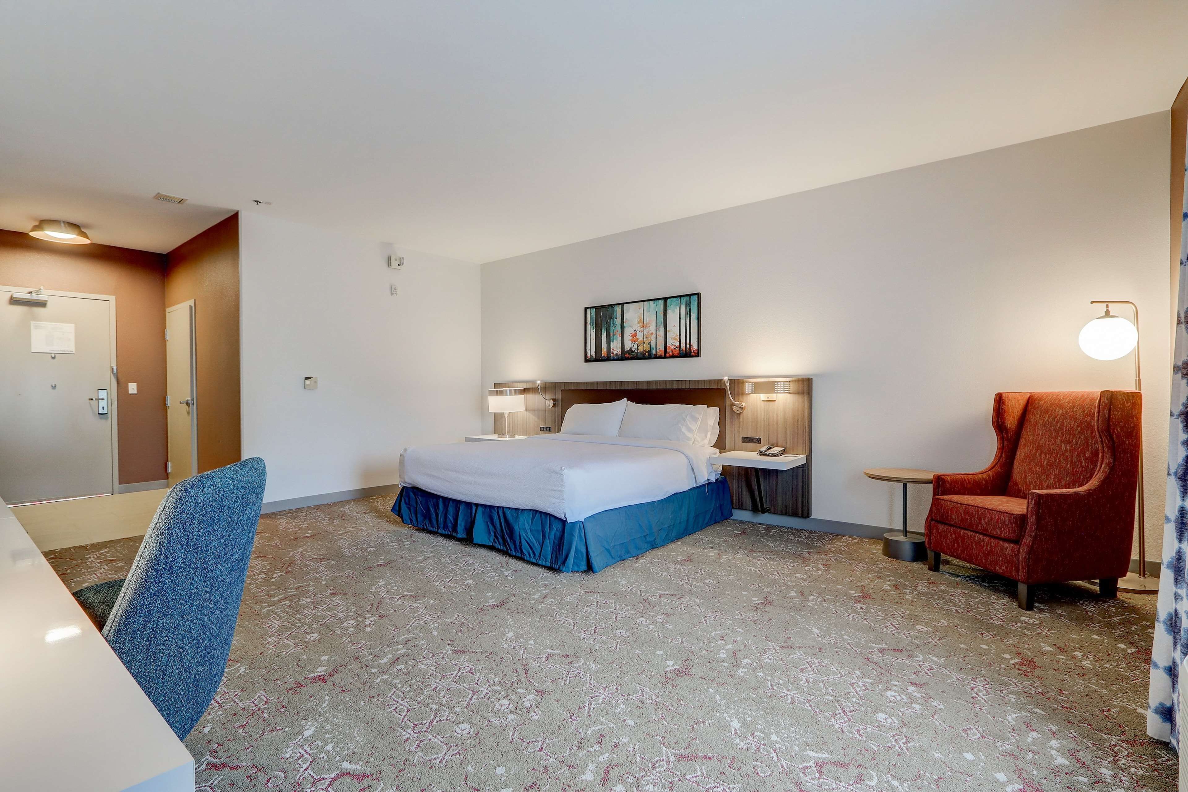 Een hotelkamer met een bed, een bureau, een stoel, een nachtkastje, een lamp en een schilderij aan de muur.