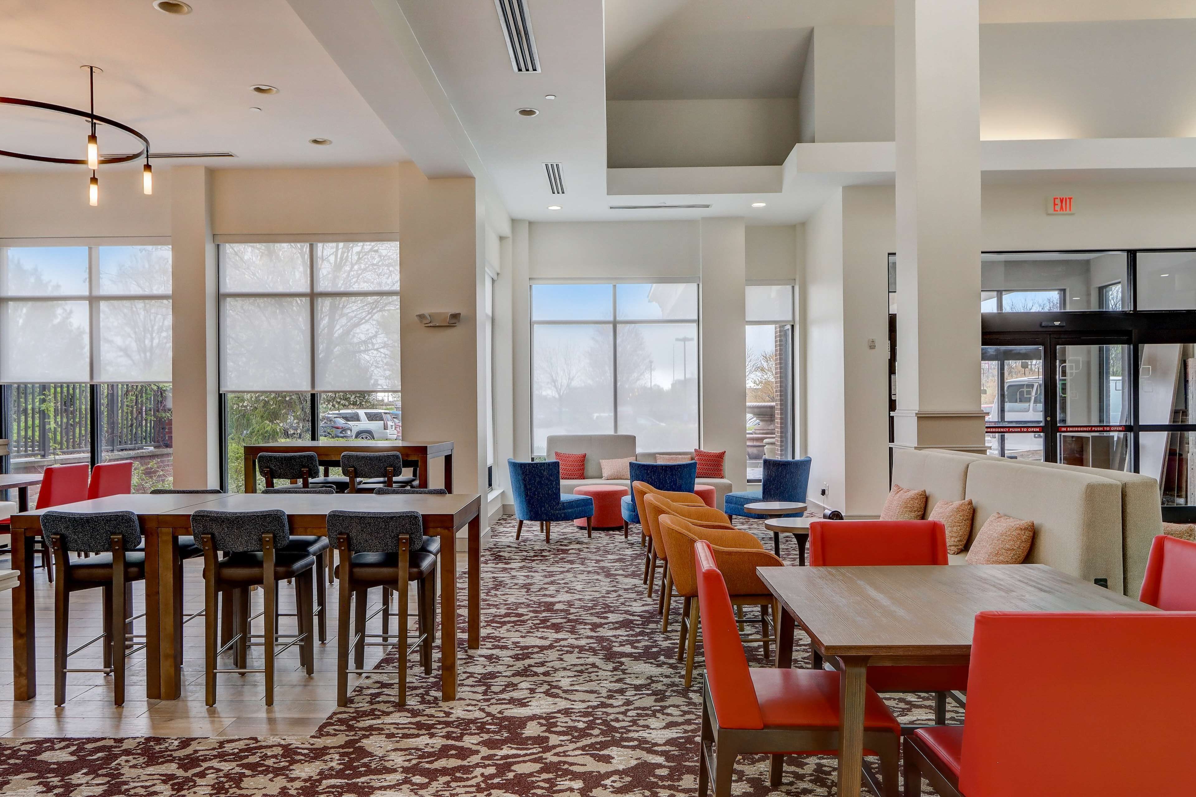 Un comedor moderno con mesas y sillas, ventanas amplias y una alfombra estampada.