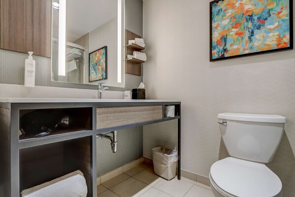 Un baño moderno con un lavabo blanco, espejo e inodoro. Hay un bote de basura debajo del lavabo y un perchero encima.