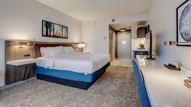 A modern hotel room with a bed, bedside table, artwork, and a reception desk. - Hilton Garden Inn Indianapolis Northwest (Indianapolis)